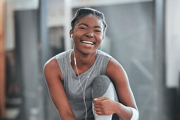 smiling black woman sitting on floor of gym with headphones on 